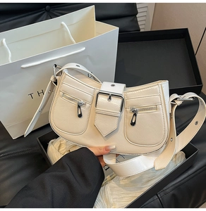 Detail of a creamy leather underarm bag featuring decorative zippers and belt buckle closure