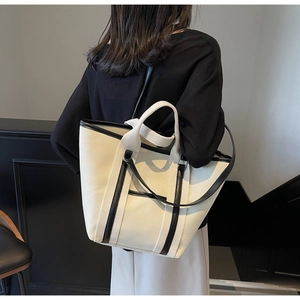 Rear view of a model carrying a large canvas tote bag with black trim and shoulder straps