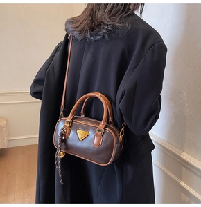 Chocolate brown leather pillow bag with gold logo shown on model wearing black coat