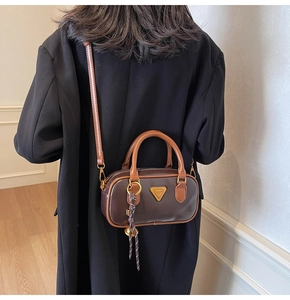 Brown leather boston bag with gold triangle logo worn crossbody over a black coat