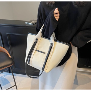 Detail of canvas tote bag with black leather handles and front pocket held by model