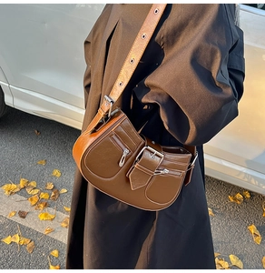 Brown vintage faux leather saddle bag worn crossbody with metallic buckle and silver zippers