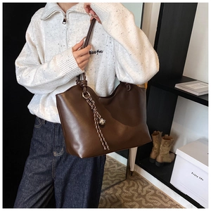 Detail of dark brown tote bag featuring decorative woven cords and sleek leather texture