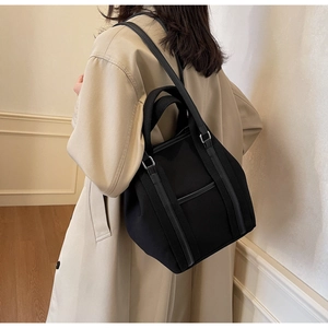 Side view of black canvas tote bag with leather handles and silver metal hardware