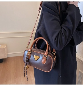 Detailed view of brown boston bag with contrast handles and metallic triangular logo