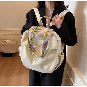 Close-up of beige nylon backpack featuring colorful woven straps and round brand logo patch