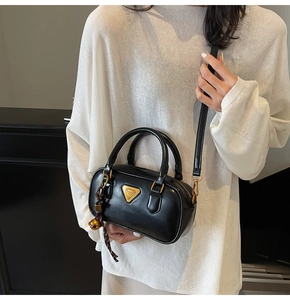 Detail of black leather handbag with golden triangle logo and bell pendant on strap