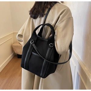 Detail of black canvas and leather tote bag worn with a casual khaki trench coat