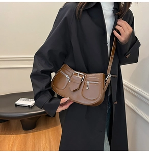 Detail of a dark brown glossy underarm bag with silver buckles on a person wearing a black coat