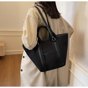 Detail of black canvas tote bag with leather straps on model in minimalist interior