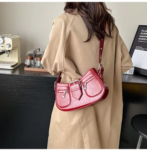 Detail of dark red underarm bag with decorative zippers and adjustable strap on a model