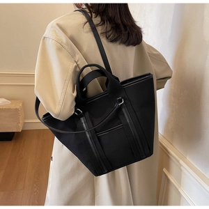 Detail of large black canvas tote bag with leather straps on model in trench coat