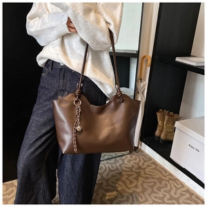 Detail of dark brown leather tote bag with wavy top edge and decorative woven charm