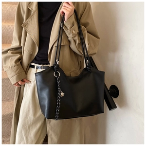 Detail of black faux leather tote bag with knot strap and tassel charm on model