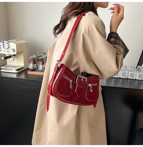 Detail of burgundy semi-circle shoulder bag with metallic zippers and wide buckle