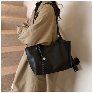 Detail of minimalist black tote bag with braided charm ornament and smooth leather texture