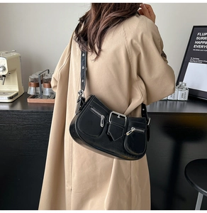 Black leather underarm bag with silver buckles shown on a model in a trench coat