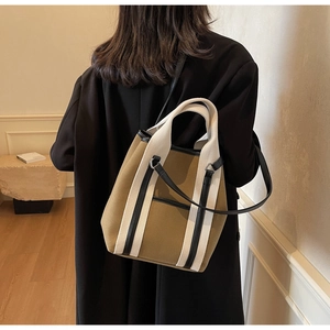 Detail of khaki canvas tote bag featuring striped webbing handles and black leather shoulder strap