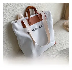 Detail of canvas tote bag showing brown leather handles and adjustable woven strap