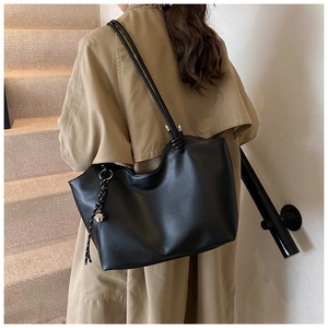 Black leather tote bag styled with a beige trench coat on a minimalist staircase