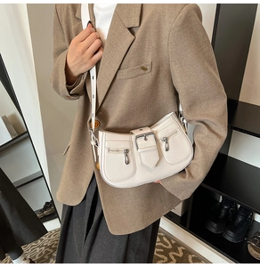 Close-up of cream underarm bag with decorative buckles and functional zip pockets
