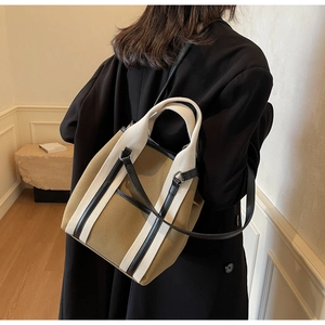 Detail view of khaki canvas tote bag with black leather straps and white trim accents