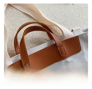 Detail of canvas tote bag showing brown leather handles with white stitching craftsmanship