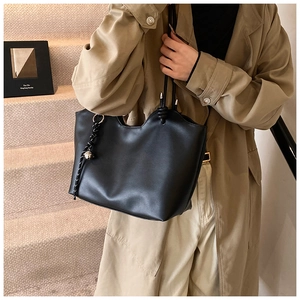 Detail of black tote bag with wavy edge and knot pendant on a beige trench coat