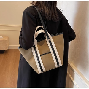Detail view of khaki canvas tote bag showing black leather trim and woven straps