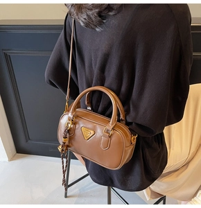 Detail of a brown leather pillow bag with a triangle metal logo and woven strap charm