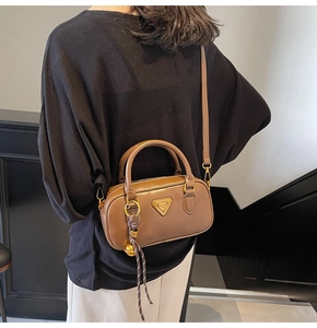 Detail shot of brown leather pillow bag with metal triangle logo and woven bell charm