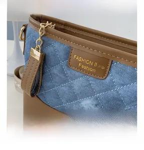 Detail of blue quilted denim cross-body bag with brown leather trim and golden logo