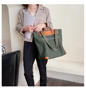 Detail of large dark green canvas tote bag with brown leather handles and shoulder strap