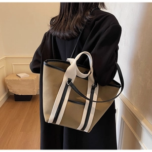 Close-up of a khaki canvas tote bag with white straps and black leather trim