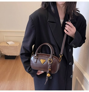 Detail of a dark brown crossbody pillow bag with gold hardware and spherical chain