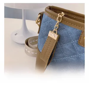 Detailed view of the smooth zipper and brown leather trim on the blue quilted denim bag