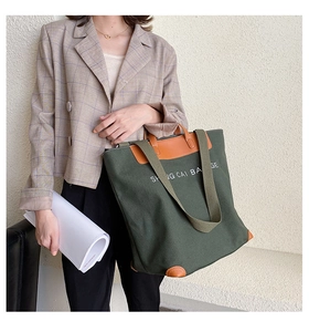 Detail of dark green canvas tote bag with brown leather handles and white text decoration