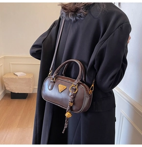 Detail of dark chocolate leather Boston bag with triangle metal logo on black coat