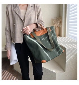 Detail of dark green canvas tote bag with brown leather handles on a model in sunlight