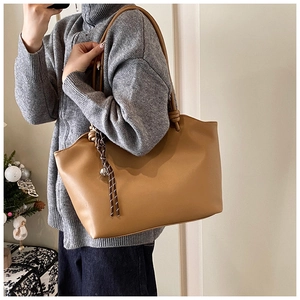 Detail of camel tote bag with brown woven tassel charm and matte leather texture