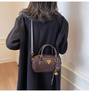 Detail of a dark brown mini pillow bag with gold triangle logo and crossbody strap