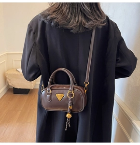 Detail view of dark brown leather pillow bag with gold triangle logo and braided pendant