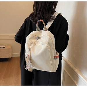 Detail view of cream backpack featuring colorful braided handles and multi-zipper layers