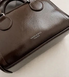 Detailansicht der braunen Kunstlederstruktur und des goldenen Logos auf der Tasche