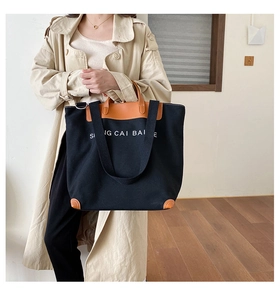 Detail of canvas tote bag with leather trim and SI NG CAI BAI E text showing straps