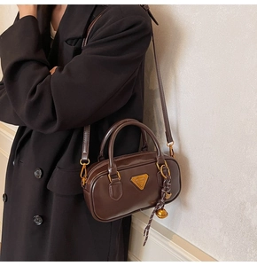 Close-up of a coffee brown leather boston bag with a triangular metal logo on black blazer