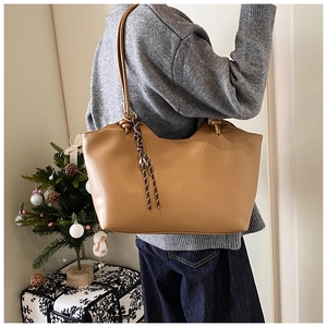 Close-up of brown tote bag with knot strap detail and woven tassel charm in cozy setting