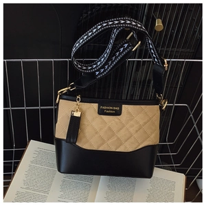 Detail of quilted khaki fabric and black leather bucket bag with wide strap and gold charm