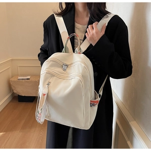 Detail view of cream travel backpack showing colorful geometric woven straps and multi-zipper pockets