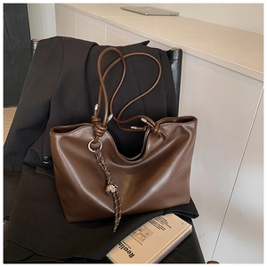 Close-up of brown tote bag featuring knot handle and woven bell charm detail